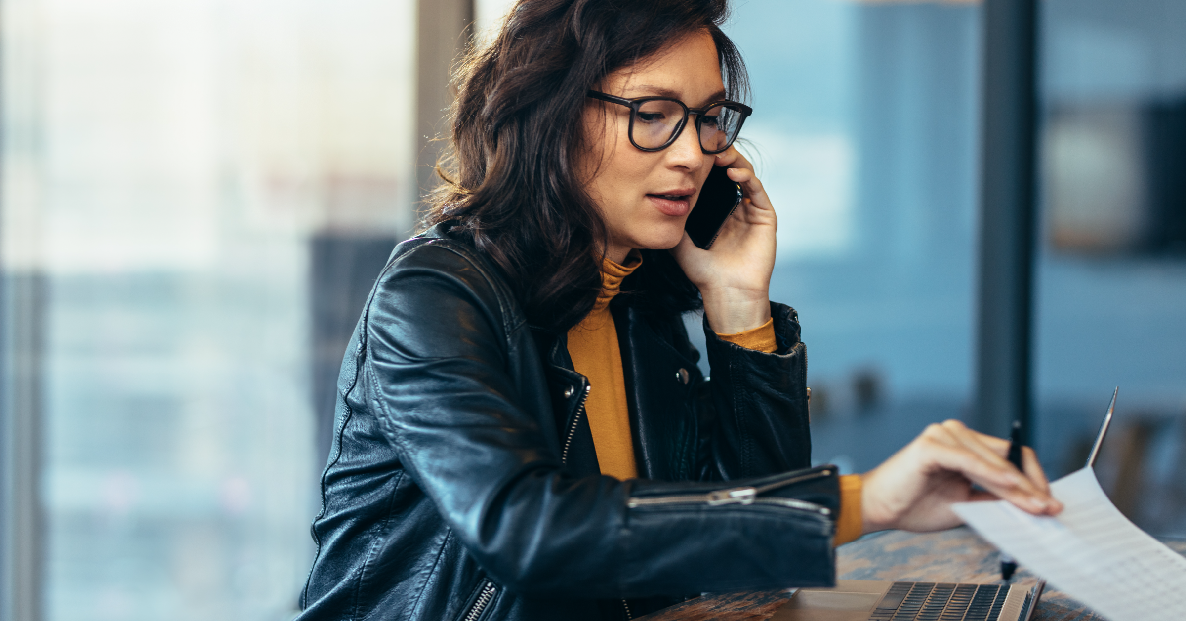 Photograph of a revenue operations leader talking on a smartphone and looking at a report in front of a laptop