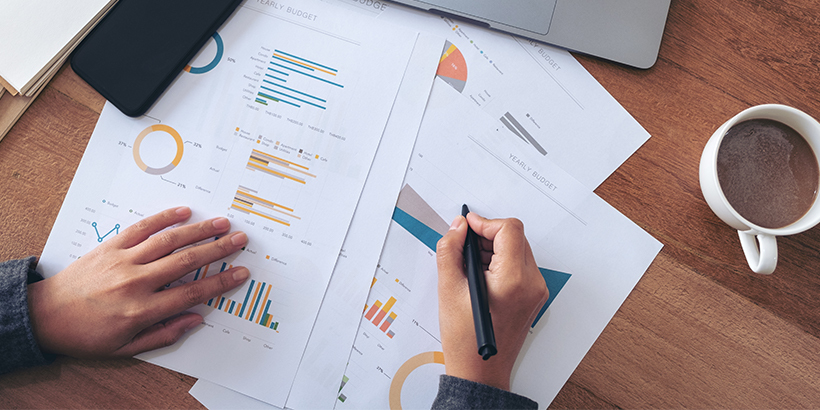 Photograph of a revenue leader's hands writing on printouts of sales forecasts next to a cup of coffee