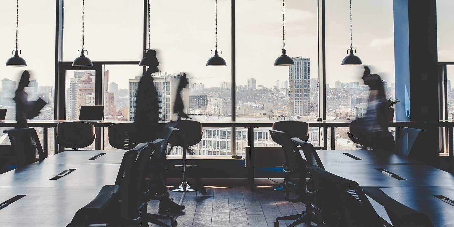 Photograph of blurred people walking through a backlit city office